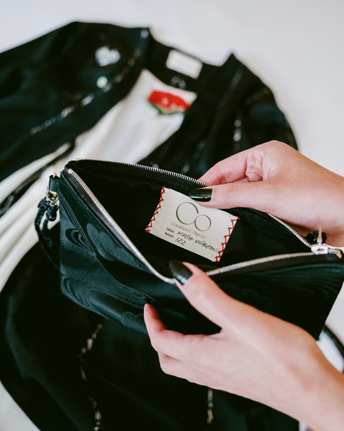A close-up of a person holding a vintage silk obi zip pouch, showing the interior lining and a sewn-in brand tag. The brand name 'Considered Objects' 
