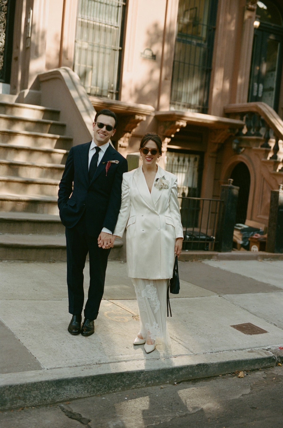 A couple standing on a city sidewalk in front of a brownstone building. The woman is wearing the Falling Flower brooch in ivory/cream.  Photography by Nicole Plett, courtesy of Kirsten McNally. 