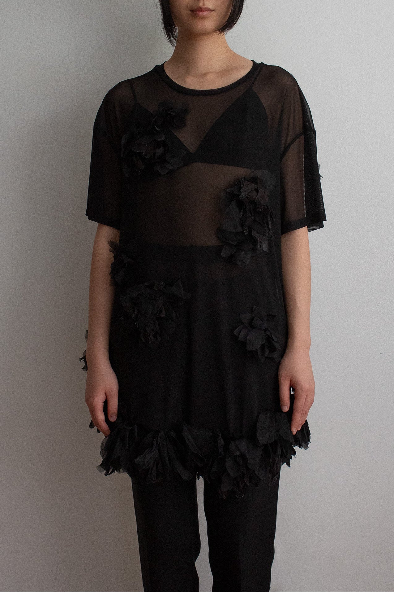 Woman wearing a black dress with floral details against a plain background