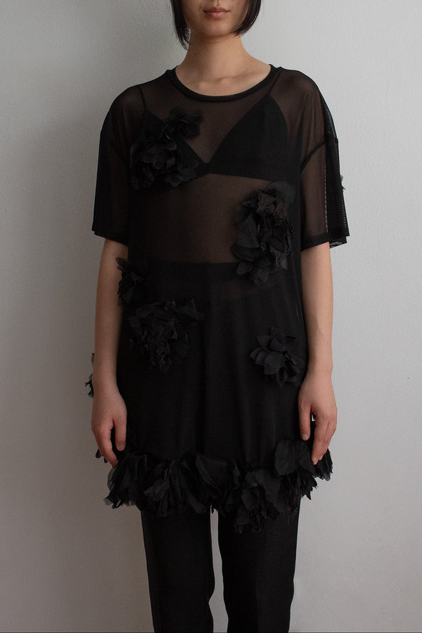 Woman wearing a black dress with floral details against a plain background