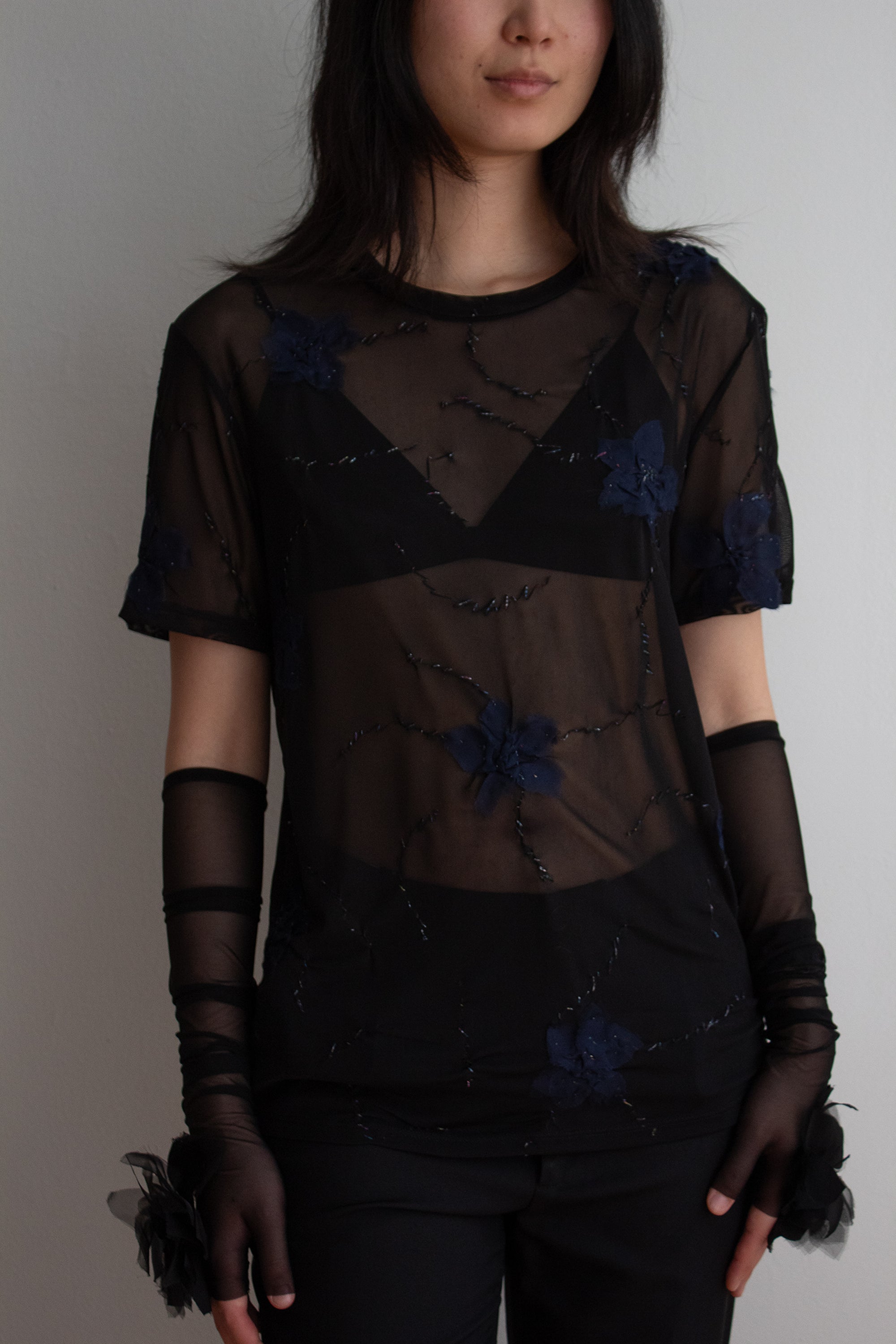 Person wearing a black sheer top with floral embellishments against a plain background