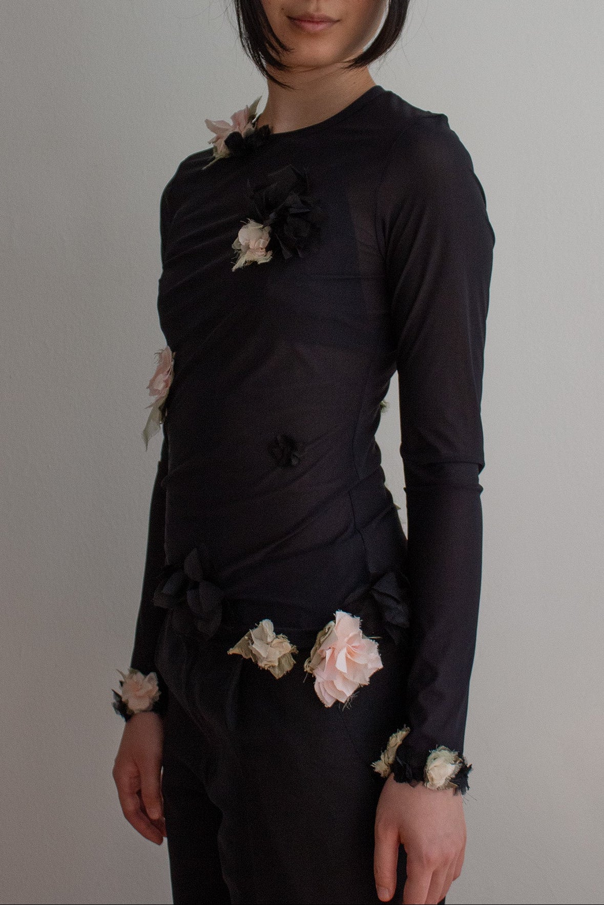 Woman wearing a black top with floral embellishments against a plain background