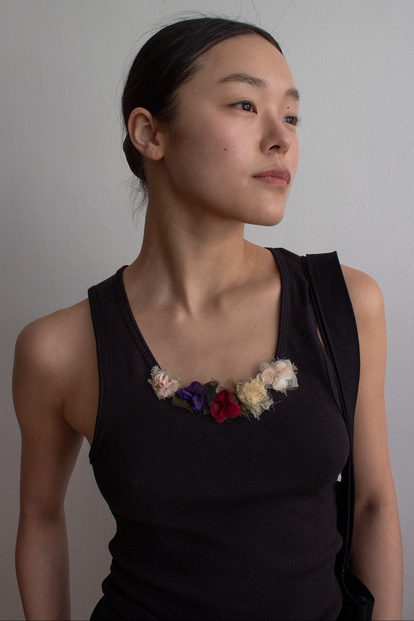 A woman wearing a black sleeveless top with a floral embellishment against a plain background
