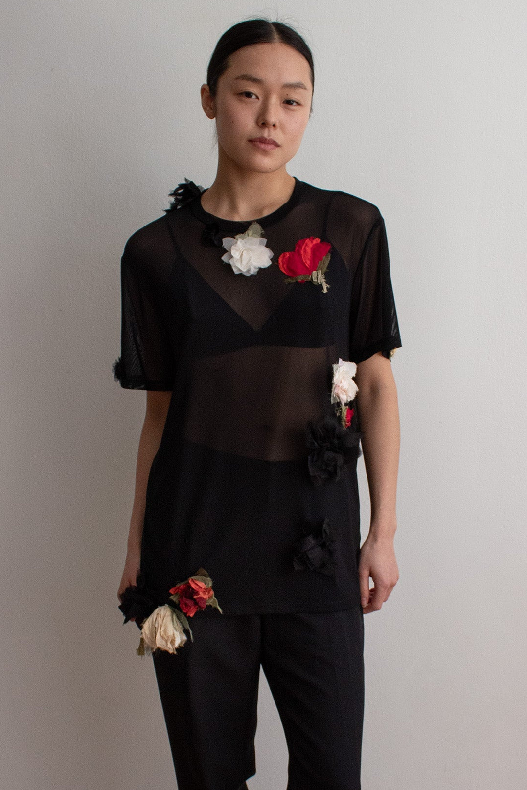 Person wearing a black outfit with floral embellishments against a plain wall.