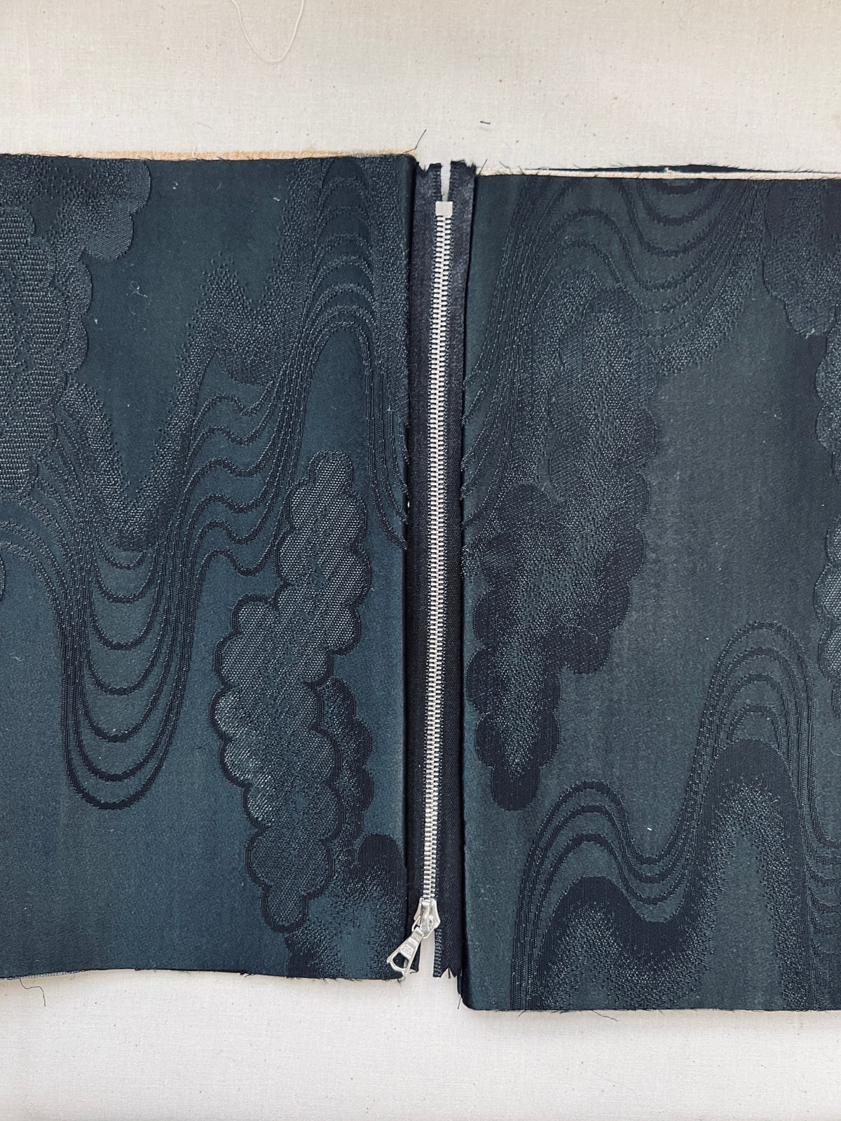 A close-up of a zipper closure on a pair of dark navy blue patterned fabric pants or shorts, showing a textured cloud-like jacquard weave.