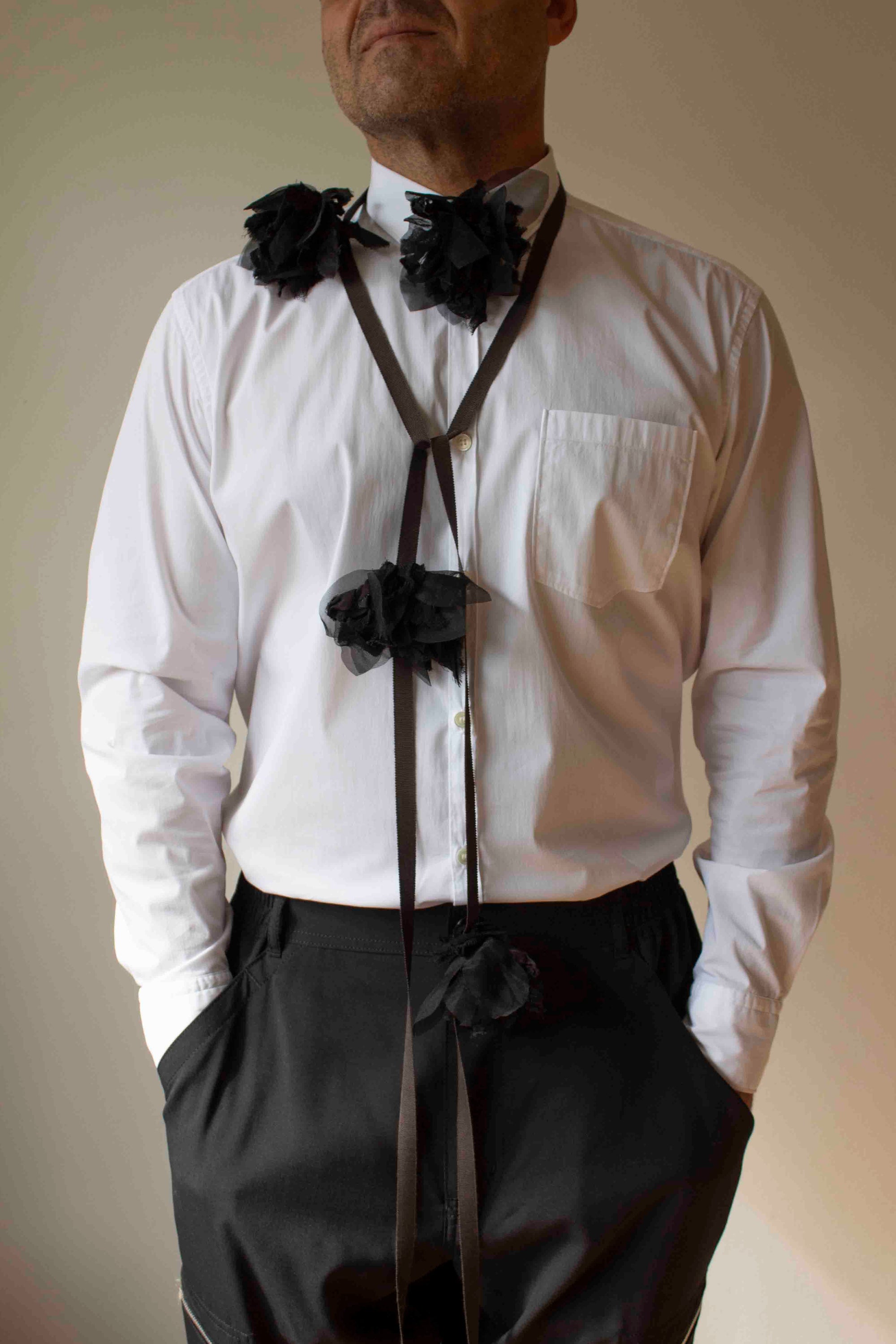 Man wearing a white shirt  and black floral attachments against a plain background
