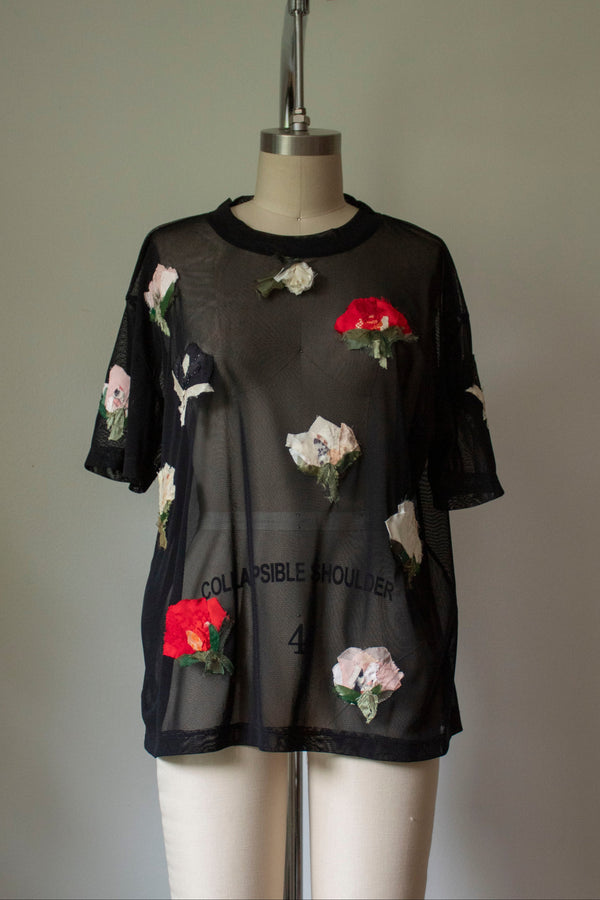 A sheer black mesh t-shirt with multicolored pressed flower embellishments on a mannequin.