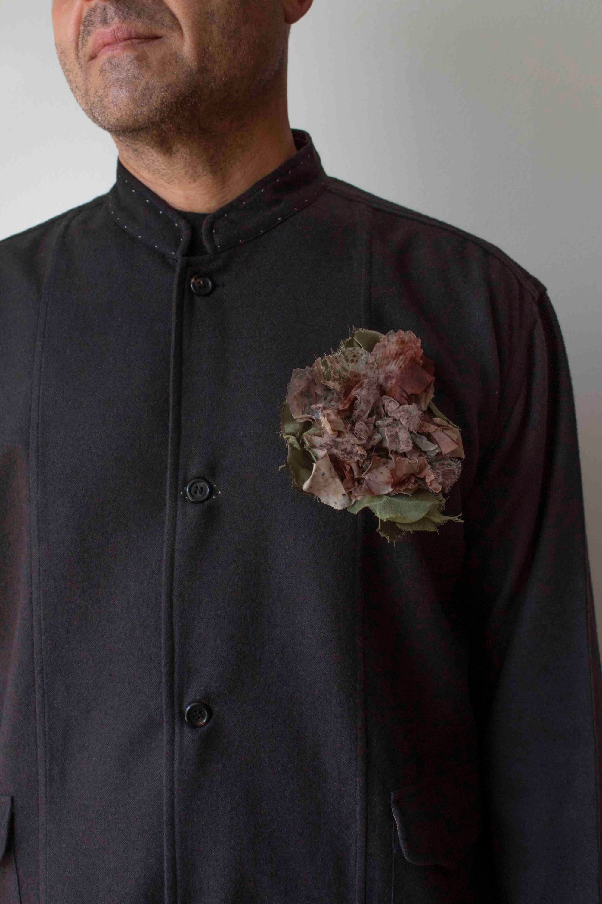 Man wearing a dark jacket with a floral boutonniere on a plain background