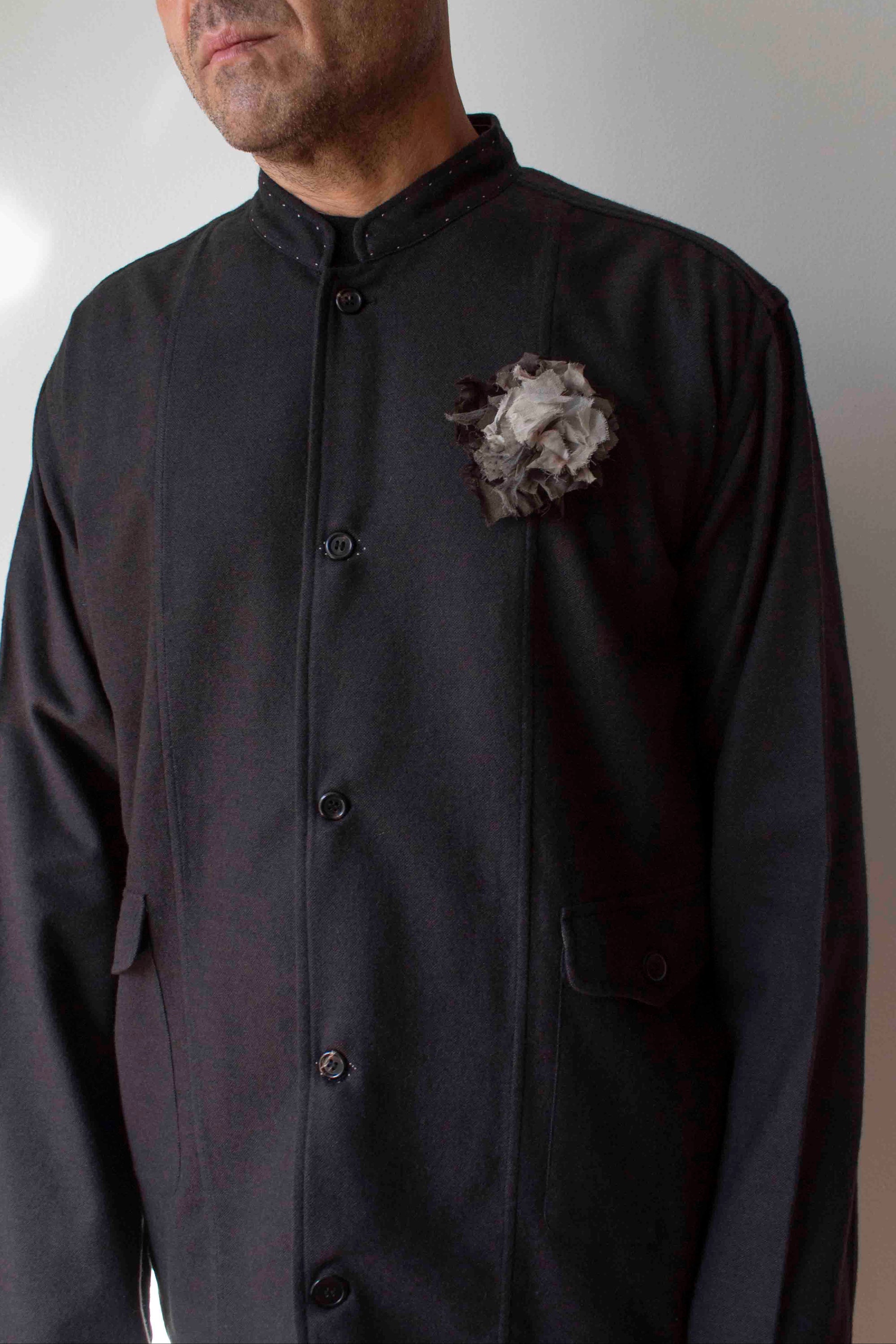 Man wearing a dark long-sleeve shirt with a floral brooch against a plain background