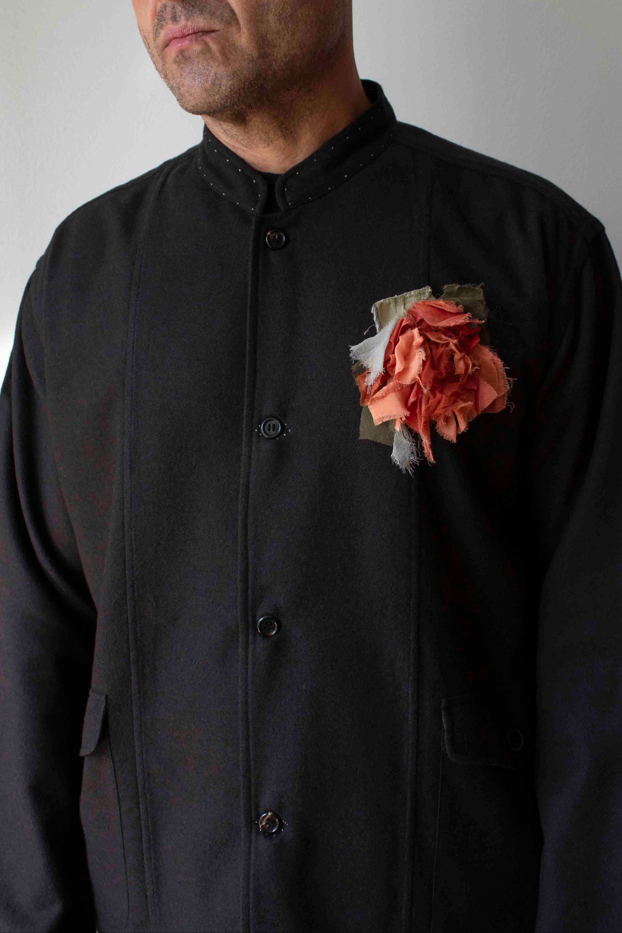 Man wearing a brown jacket with a floral brooch against a plain background