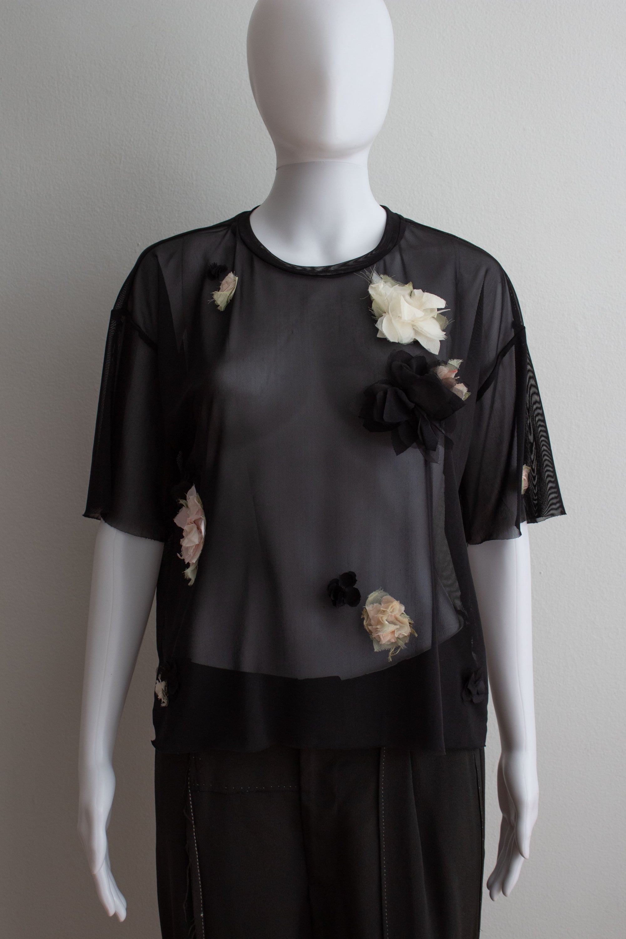 Mannequin wearing a black outfit with floral embellishments on a plain background