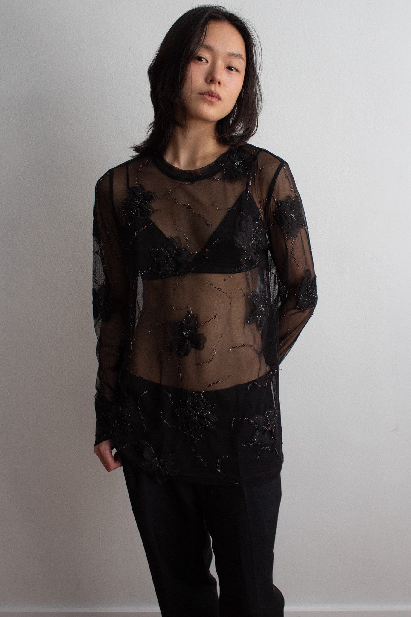Person wearing a sheer black long-sleeve top with floral patterns against a plain background