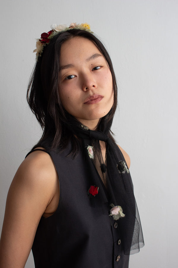 Woman wearing a black sleeveless top with floral details against a plain background